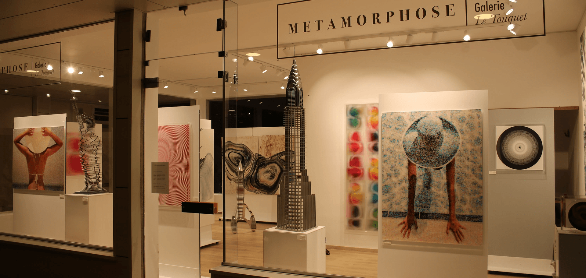 Gallery window display with various colorful artworks and sculptures under bright lighting.